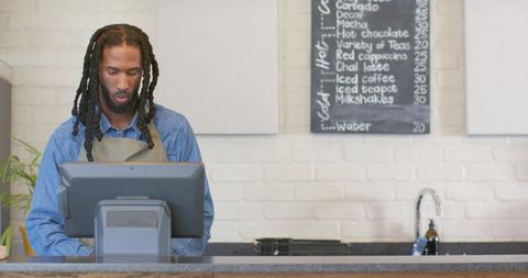 African american barista using touchscreen pos at cafe counter in denim and apron