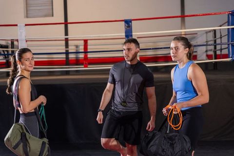 Male trainer coaching two women athletes in boxing ring during resistance band workout