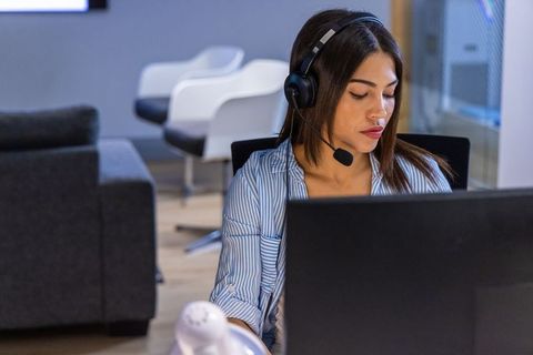 Asian customer service agent wearing headset working at laptop in modern open-plan office