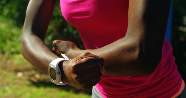 Image shows close-up view of a fit woman stretching arms outdoors wearing a pink top and a smartwatch. Great for promoting fitness routines, healthy lifestyle products, workout tips, and wearable fitness technology.