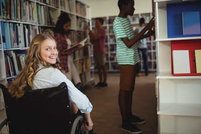 Disabled girl in wheelchair smiling in school library with other students reading books. Ideal for educational materials, diversity and inclusion campaigns, and accessibility awareness.
