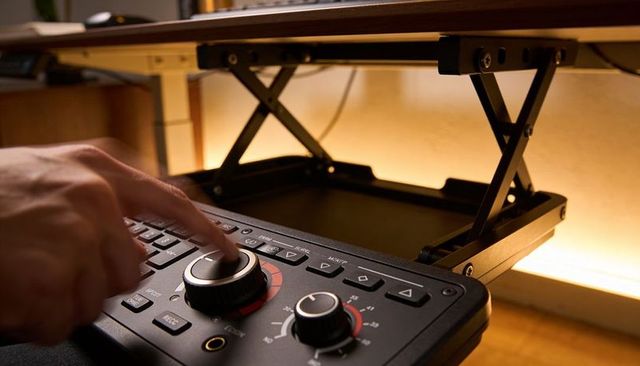 Pressing knob on audio controller while adjusting scissor-lift desk riser in wooden studio