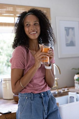 Smiling african american woman holding orange juice leaning on countertop in kitchen