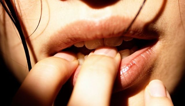 Close-up of woman biting fingernails revealing front teeth and glossy lip scab