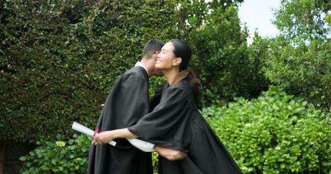 Joyful graduation celebration of young couple outdoors in caps and gowns
