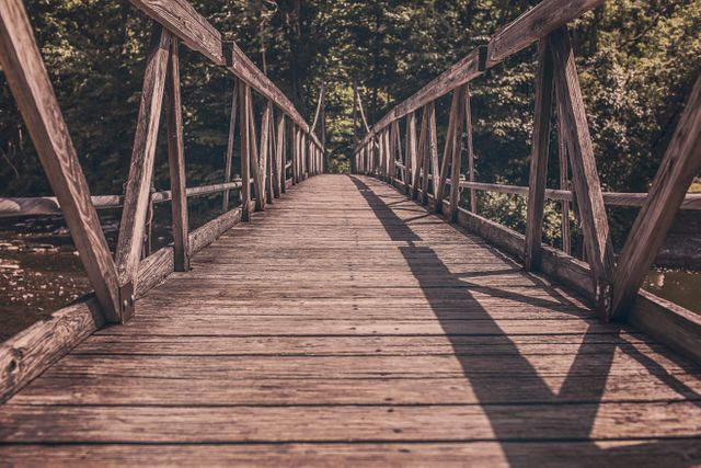 Capturing a serene wooden bridge under the gentle sunlight in the midst of a dense forest. Great for use in travel blogs, nature documentaries, promotional materials for hiking trails, and personal relaxation projects. Evokes a sense of calm, exploration, and connection with nature.