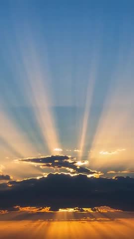 Sun peeking behind clouds casting crepuscular rays over golden ocean sunrise vertical