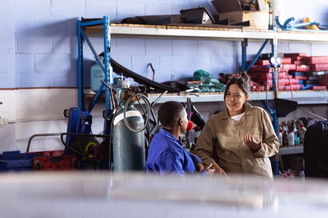 Female asian welder talking with mid adult african american colleague while working in car workshop. Unaltered, copy space, welding, occupation, industry, engineering, manufacturing, teamwork.
