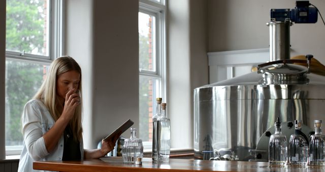 Woman in modern distillery examining and tasting alcoholic beverages. Perfect for content related to craft alcohol production, quality control processes, small business operations, and female professionals in industry.