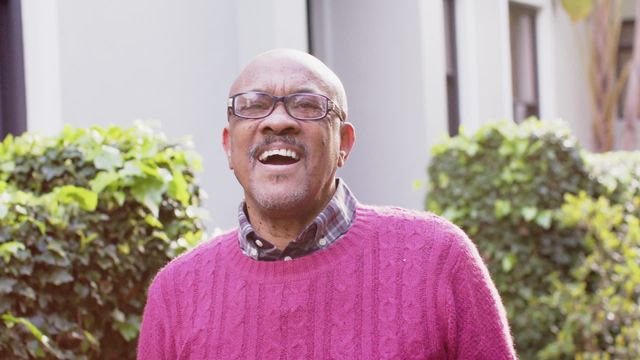 Elderly man enjoying a moment of joy outdoors, wearing glasses and a pink sweater. Perfect for content related to senior lifestyle, happiness, well-being, retirement living, or promoting joyful living among the elderly.