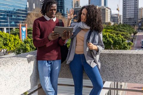 Diverse young professionals collaborating on tablet at urban overlook with city skyline