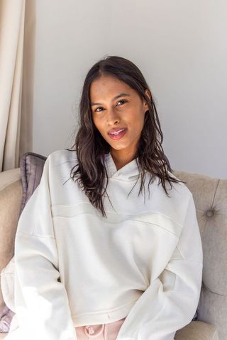 Young woman relaxing on beige sofa wearing cream hoodie and pink loungewear