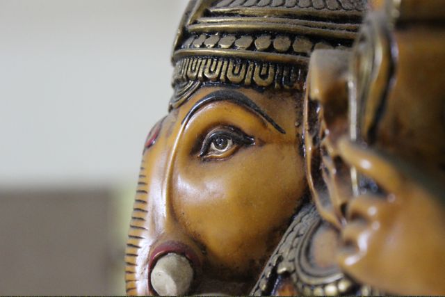 Detailed close-up shot of a traditional Ganesha statue showcasing intricate craftsmanship. Highlight on golden tones and elaborate carvings, making it ideal for projects related to Indian culture, religious studies, traditional artwork, and decorative motifs.