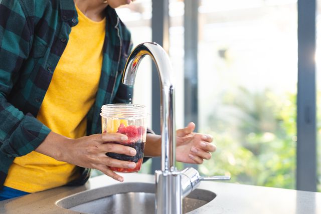 Man washing fresh fruit under faucet in modern kitchen. Ideal for content related to healthy living, home routines, self-care, and domestic life. Suitable for blogs, articles, and advertisements promoting healthy eating, kitchen appliances, or home improvement.