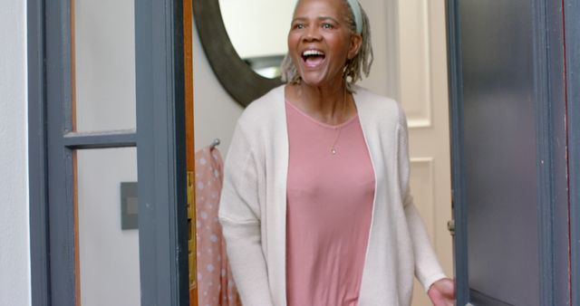Happy senior african american woman welcoming at her front door, slow motion. Home, retirement, wellbeing, domestic life and senior lifestyle, unaltered.