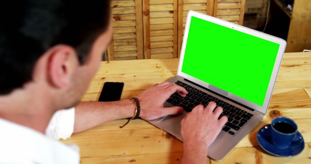 Man working on laptop with green screen in cozy cafe - Download Free Stock Images Pikwizard.com