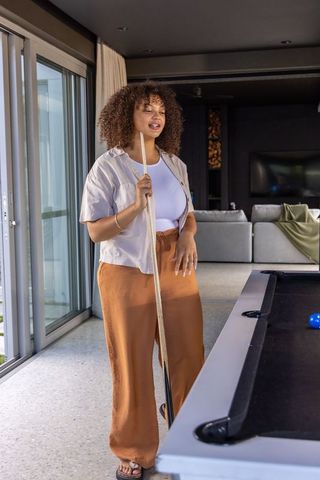 African american woman relaxing by pool table holding cue in modern minimalist lounge