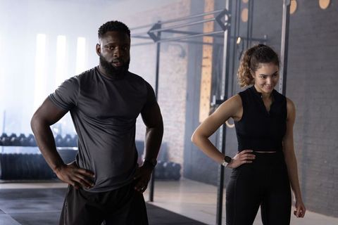Diverse fitness duo standing with hands on hips in industrial gym preparing workout