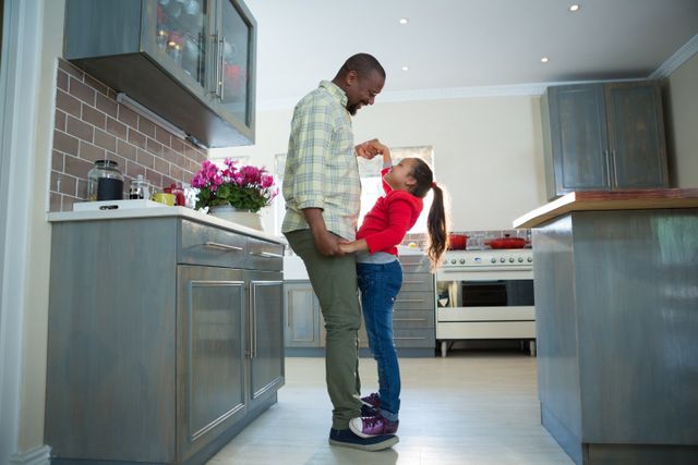 Smiling father and daughter dancing together in kitchen
