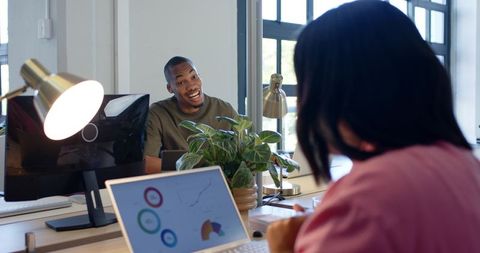 Coworkers collaborating at open-plan desk with laptop charts and natural light