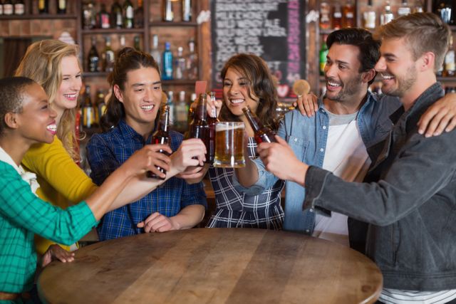 Cheerful friends toasting beer glasses and bottles at table in pub