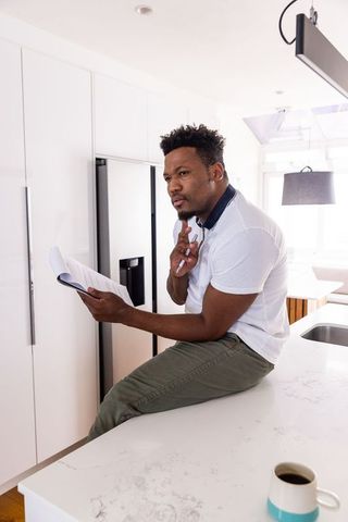 African american man reviewing papers while sitting on modern kitchen island with coffee
