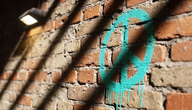 Teal peace symbol dripping on weathered brick wall with alley lamp and dramatic shadows