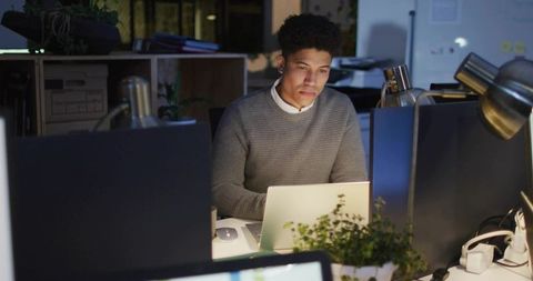 Focused young professional working late at office desk under lamp light evening productivity
