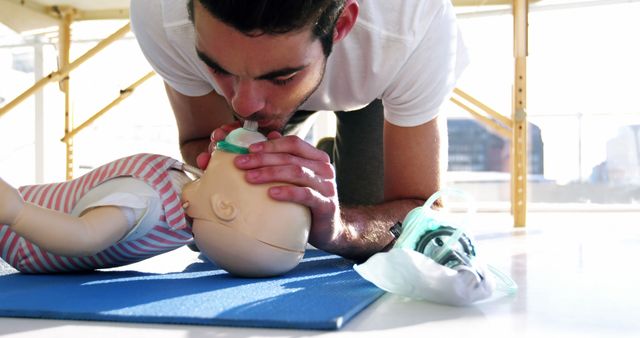 A young Caucasian man is practicing CPR on a baby mannequin, with copy space. His focused expression and the presence of a resuscitation mask suggest a first aid training session.