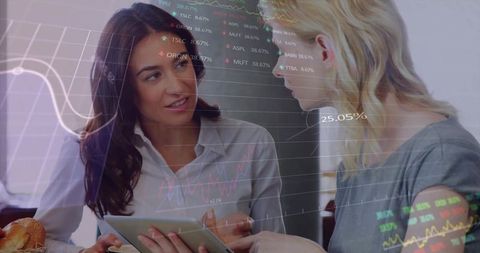 Two professional women reviewing tablet analytics in cafe with data overlay and charts