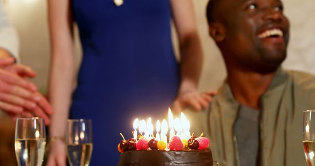 African American man enjoying a birthday celebration with a cake on the table, with copy space. Joy and festivity are evident as he looks up with a bright smile, surrounded by friends and a sense of warmth.