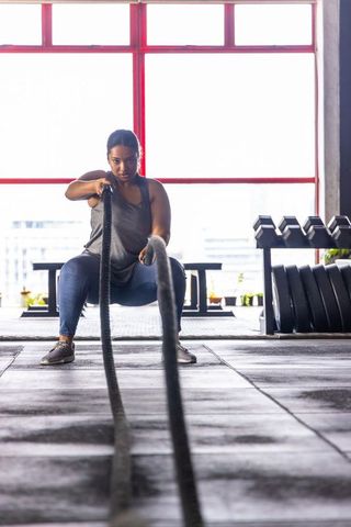 African american woman pulling battle ropes during intense squat workout in urban gym
