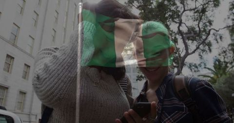 Two Friends Sharing Smartphone Moments Under Flag in Urban Area