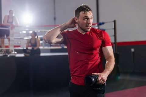 Male boxer catching breath after sparring in gym with training partners and dramatic backlight