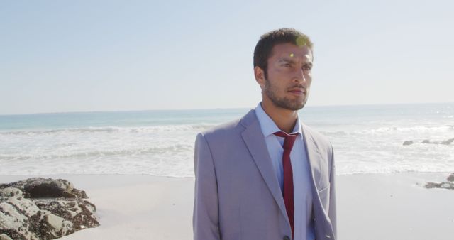 Young biracial man in a suit stands on the beach, with copy space. His professional attire contrasts with the casual outdoor setting.