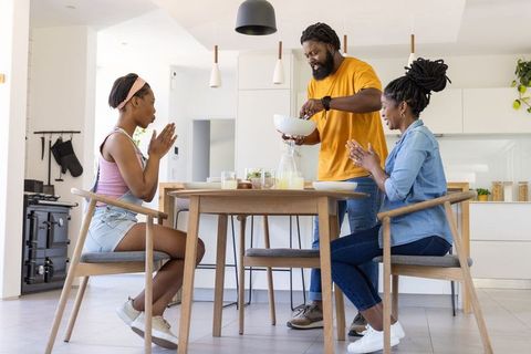 Family serving breakfast together around wooden dining table in bright modern kitchen