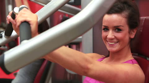 Smiling Woman Exercising on Weight Machine in Gym