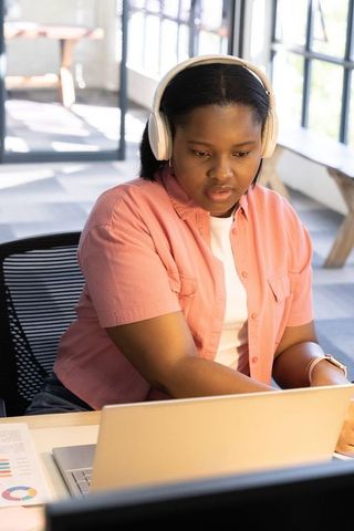 Teen african american female studying with headphones using laptop in bright workspace