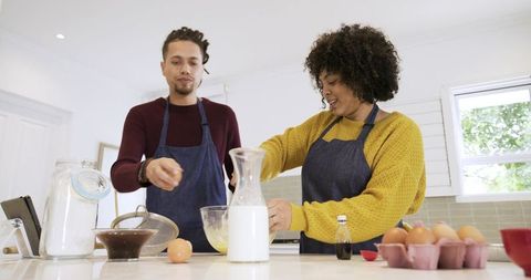 Couple baking together in modern kitchen cracking eggs whisking batter