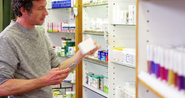 Middle-aged man scanning product in pharmacy using smartphone. Shelves are stocked with various medications and healthcare products. Can be used for topics related to technology in healthcare, modern pharmacy experience, or medication management.