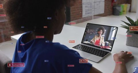 Watching virtual presentation on laptop with floating social UI icons in coworking office