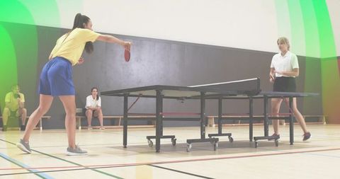 Serving player striking ping pong ball during competitive table tennis match in gym