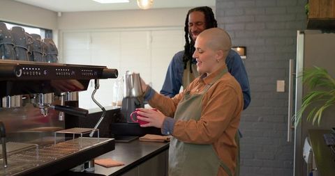 Diverse baristas steaming milk and pouring latte art behind modern espresso machine