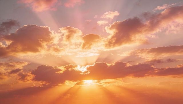 Sunrise rays radiating through layered clouds over pastel sky and tranquil horizon