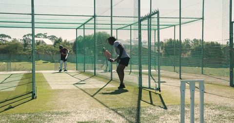 Cricket net training, bowler delivering fast balls, batsman practicing shots, teammates in nets