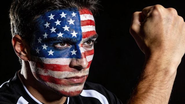 Gazing man with american flag face paint raising clenched fist, patriotic determination