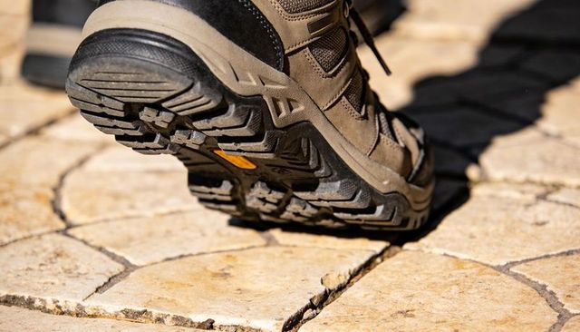 Hiking boot stepping on stone pavement close-up showing rugged tread and outdoor grip