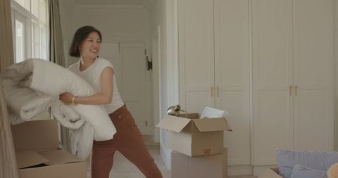 Woman Packing Bedding in Sunlit Room with Moving Boxes Nearby