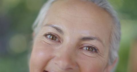 Senior woman smiling and making eye contact outdoors with soft green bokeh background