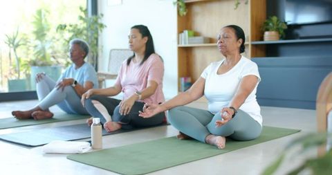 African american senior women meditating together on yoga mats in bright wellness studio